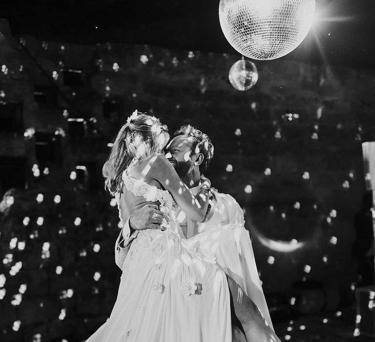 Groom lifts the bride for their first dance together with the disco ball shining 