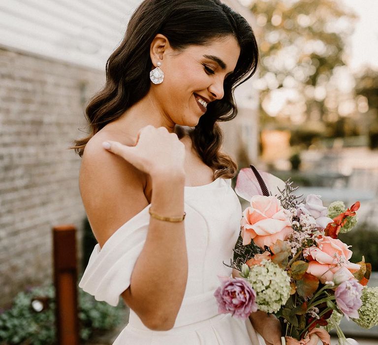 Bride with pearl earrings holding a pretty colourful wedding bouquet with pretty Hollywood waves