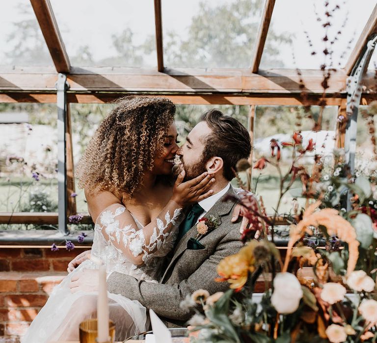 Bride sits on the groom's lap for their glasshouse reception 