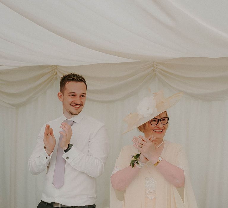 Wedding guests clap and applaud during the wedding speeches in the luxury white marquee 