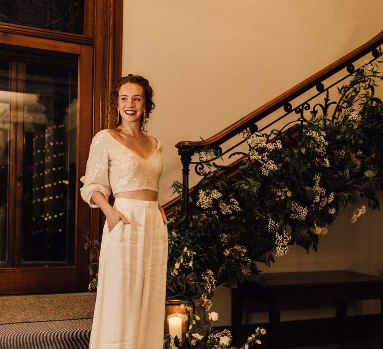 Bride in two piece bridal outfit with sparkly cropped v neck top and flowy maxi skirt standing on the stairs