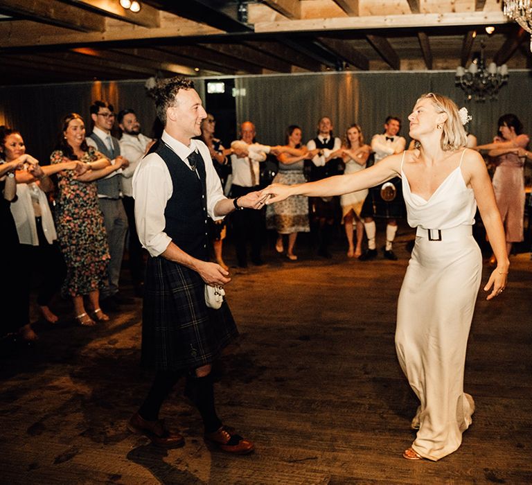 Bride in silk slip wedding dress with belt dances with her groom during wedding reception 