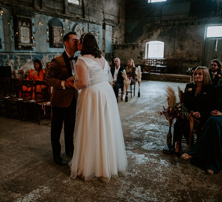 Bride and Groom share a kiss at alter in London venue decorated with fairy lights