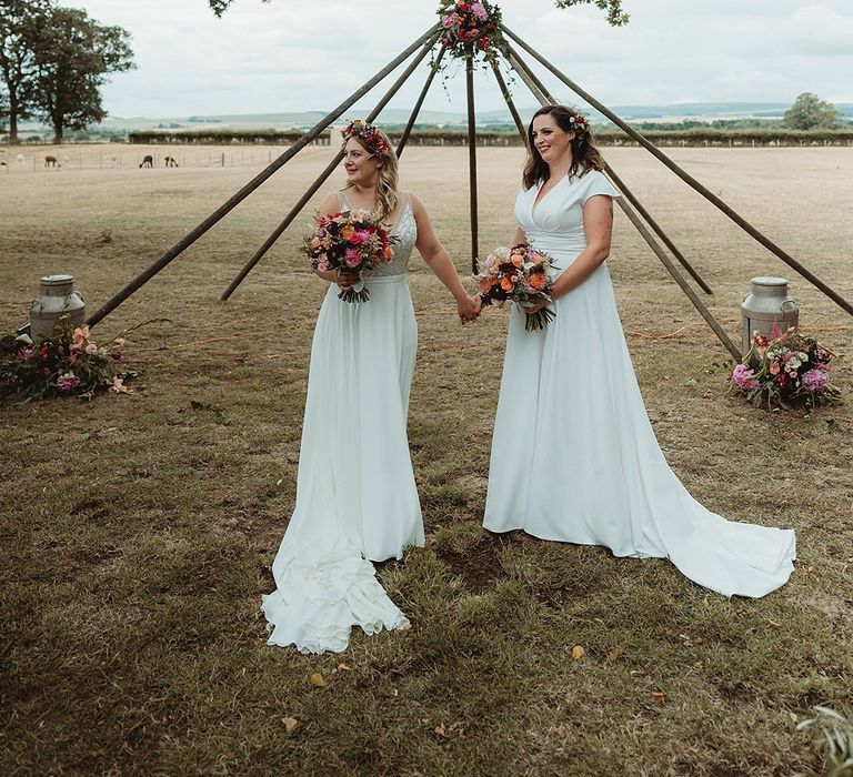 Bride in Freda Bennet wedding dress with bride in Justin Alexander wedding dress wearing flower hair accessories with bouquets and boho altar decor