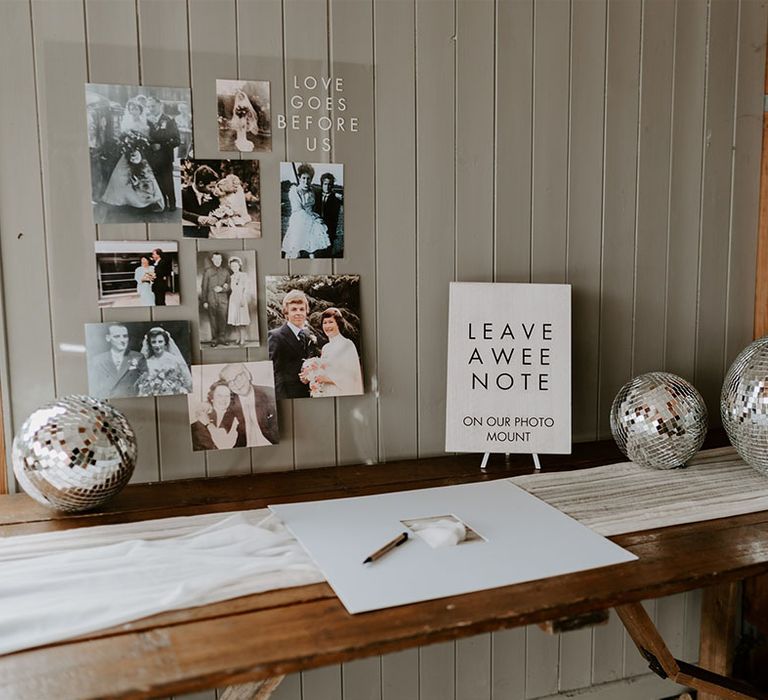 Wedding guest on wooden table with white table runner and disco balls with photos of family weddings and a black and white sign with Scottish dialect