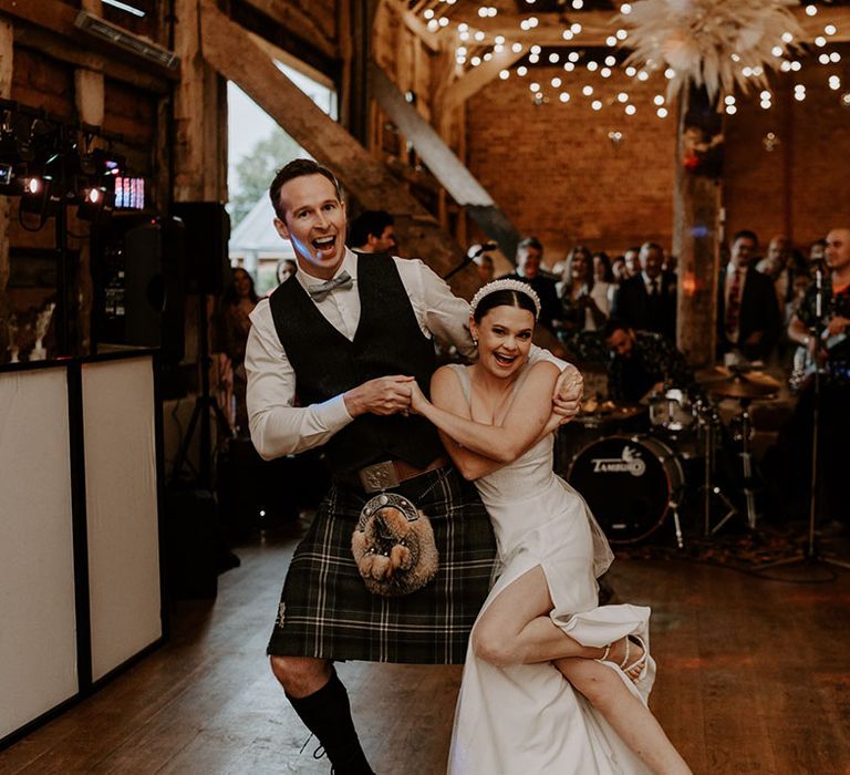 Groom in waistcoat and kilt shares the first dance with the bride in a sparkly wedding dress with a sleek updo hairstyle 