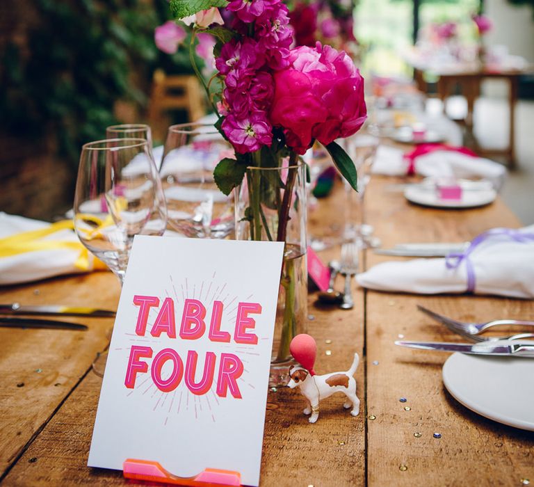 Tall thin vase with fuchsia hoary stock and hot pink peony behind pink retro wedding table number and small dog toy decoration