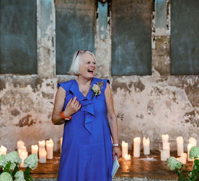 Wedding guest in purple stands in front of pillar candles during ceremony 