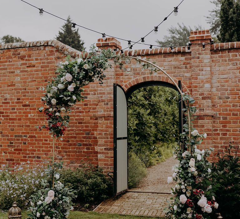 Pink and red floral arrangements beside brass lanterns outdoors 