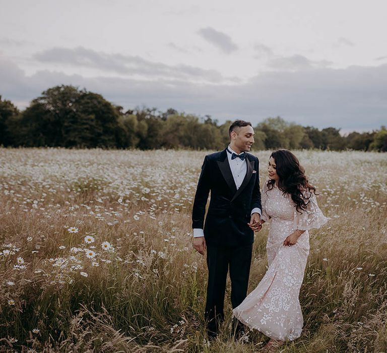 Groom in blue velvet tuxedo stands beside his bride in Needle & Thread dress