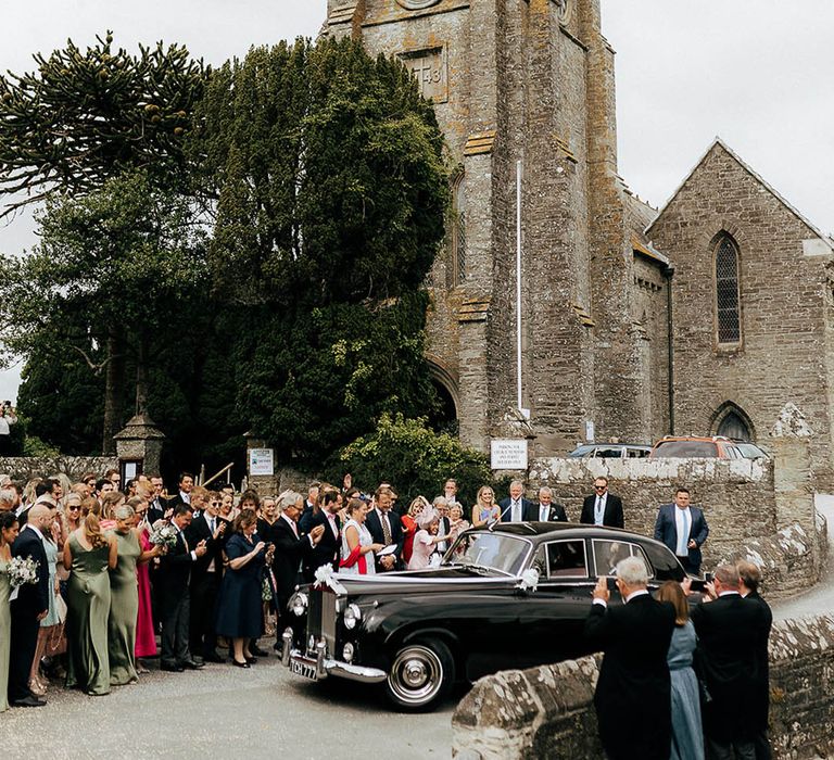 Vintage black wedding car beside wedding guests for church ceremony 