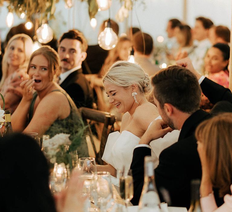 Bride laughs during wedding reception in marquee complete with green foliage installations 