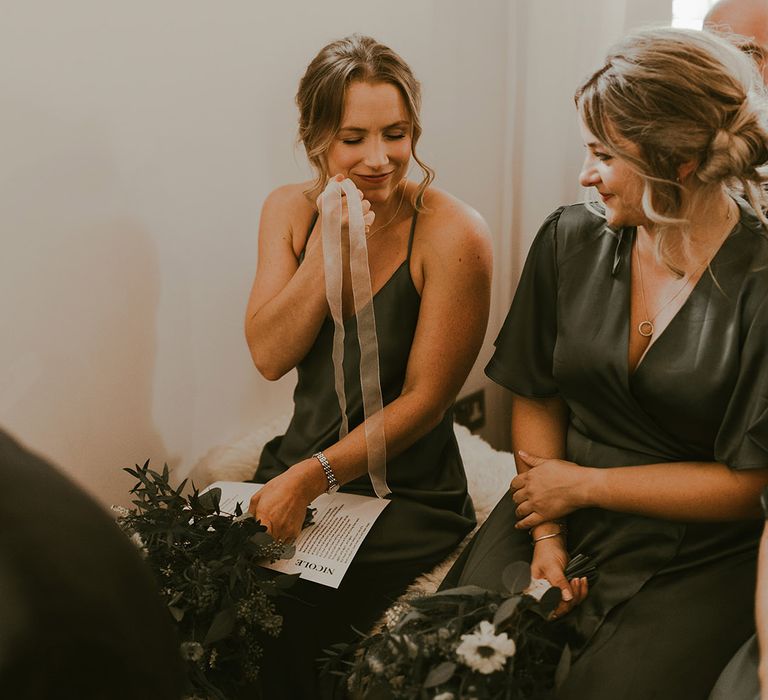 Bridesmaids in satin dark green bridesmaid dresses holding the bride's wedding ring on sheer ribbon for the ring warming ceremony 