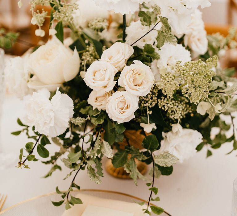 Textured style plate with gold rim with fabric napkin tied with brown string alongside white floral arrangements 