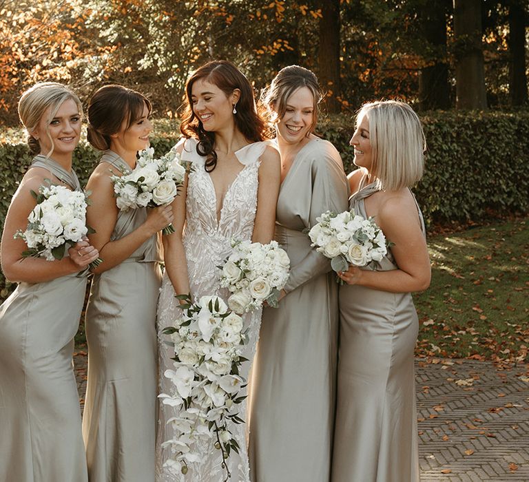 Bridesmaids in sage green satin bridesmaid dresses holding white round bouquets smiling with the bride for bridal party photos 