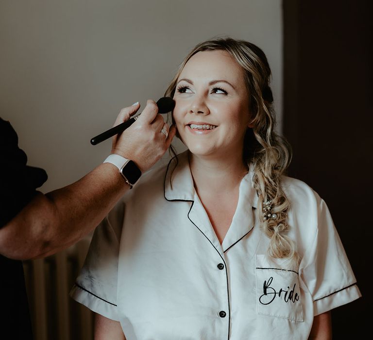 Bride wears white pyjamas whilst having her makeup done on the morning of her wedding day