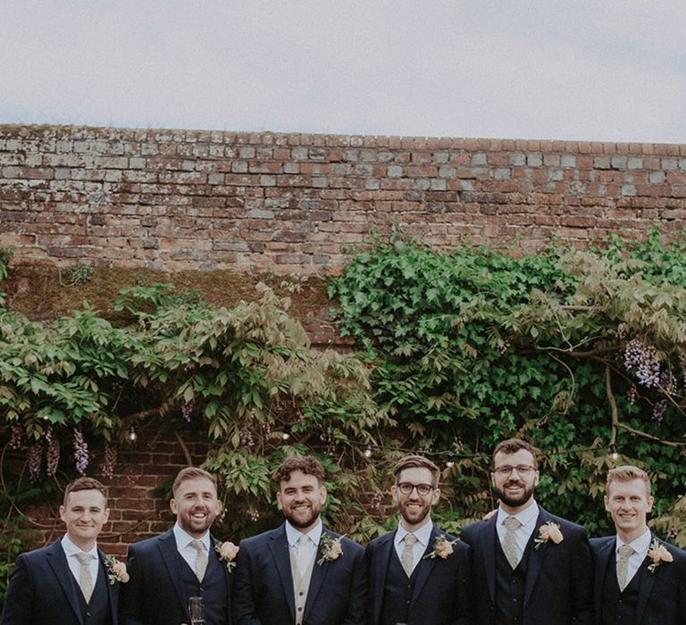 Groomsmen group party photo with the groomsmen in matching navy three piece suits with patterned ties next to the groom in a navy suit jacket with light waistcoat and pale tie 