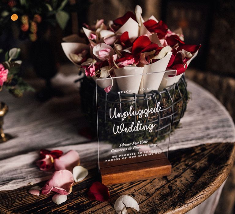 Acrylic wedding sign for unplugged wedding ceremony with basked full of confetti cones of flower petals 