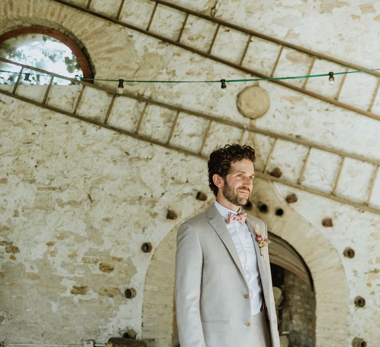 Groom in greige suit and colourful bow tie at rustic wedding venue in Italy