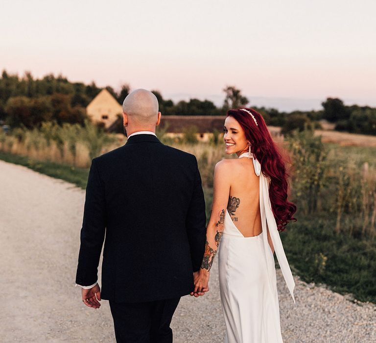 Groom in black tux with the bride in a classic low back wedding dress with halter neck style and white headband 