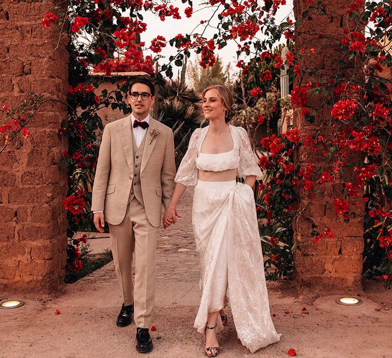 Bride in lace long sleeve crop top and maxi skirt with the groom in three piece cream suit 