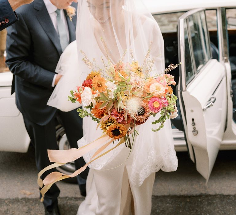 Bride wearing delicate lace veil getting out of the Rolls Royce wedding car on the way to the church ceremony 