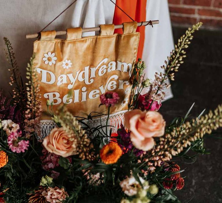 Mustard yellow velvet wedding banner on retro wedding tablescape next to large mixed flower colourful arrangement 