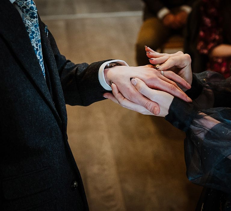 Bride with black French tip wedding nails decorated with star nail art slides the wedding ring onto the groom's finger 