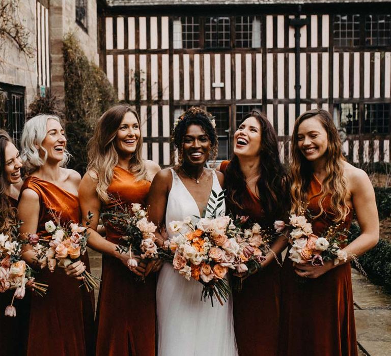 Bridesmaids in one shoulder burnt orange bridesmaid dresses holding blush and orange garden roses, poppies and carnations, dried flowers and eucalyptus wedding bouquets standing with bride in v-neck sleeveless wedding dress with 3D floral applique train at Brinsop Court wedding