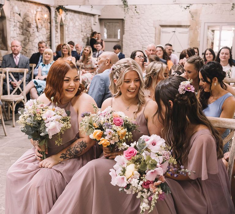 Bridesmaids sat at the wedding ceremony in pink bridesmaid dresses with pastel wedding bouquets 