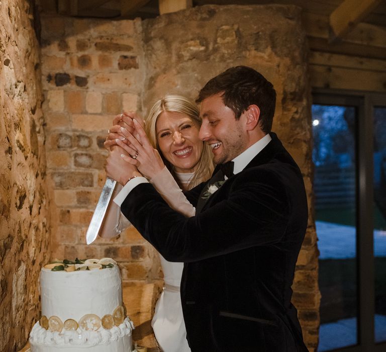 Bride and groom cut their two tier white iced wedding cake with lemon slices 