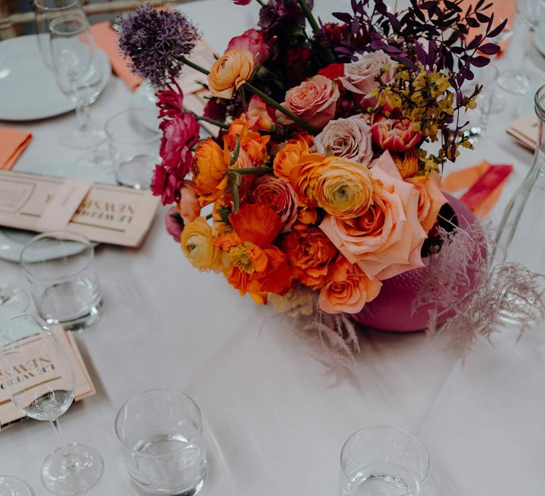 Classic wedding tablescape with colourful wedding flower centrepieces with peach, pink and blush garden roses, dried flowers and foliage, newspaper wedding menus and orange wedding napkins