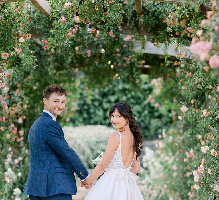 bride in an appliqué wedding dress with detachable bridal skirt holding hands with her groom in a navy check suit at Euridge Manor 