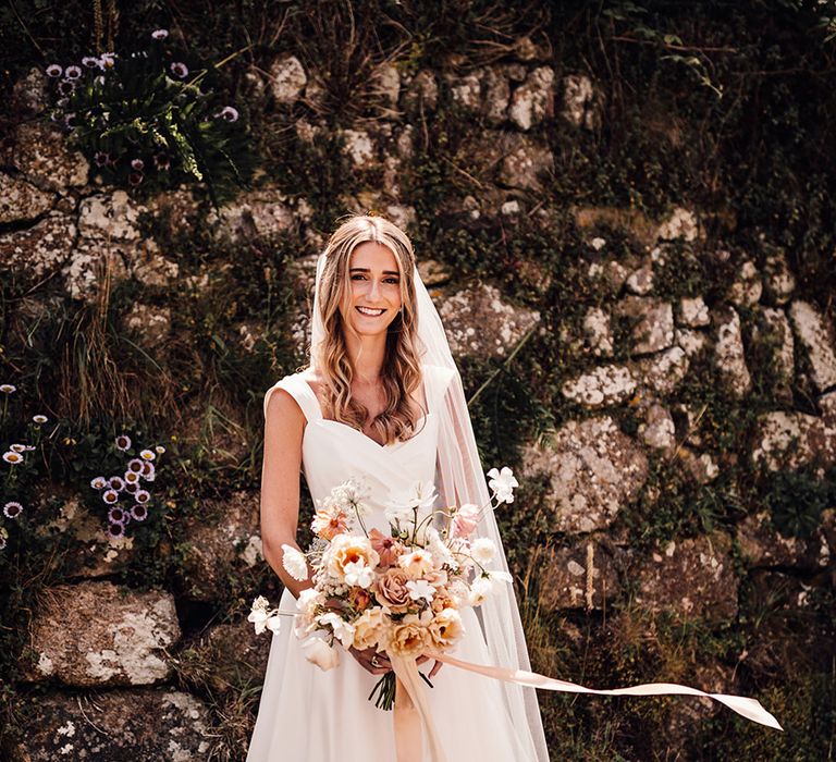 bride in a Suzanne Neville princess wedding dress holding a blush pink wedding bouquet tied with ribbon