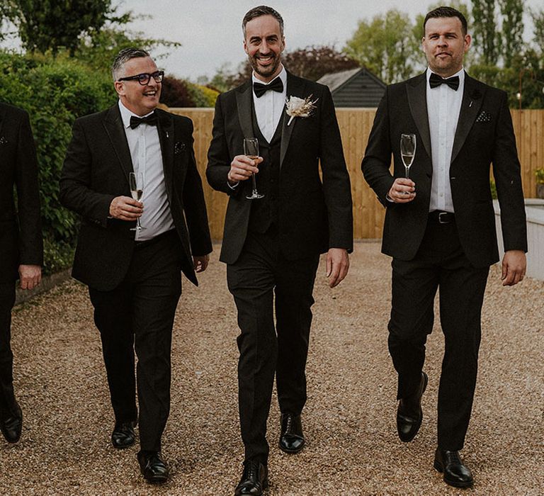 Groom and groomsmen walking to the wedding in matching black tuxedos 