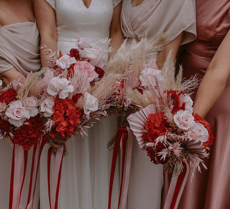 Bridesmaids and bride hold out their matching pink and red wedding bouquets 