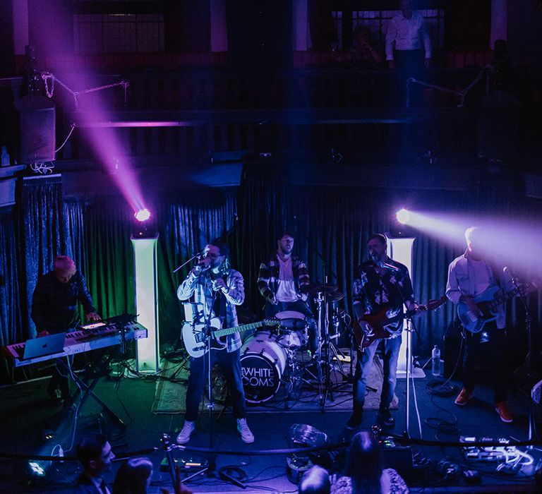 The wedding band play live music under the huge disco ball with colourful lights 