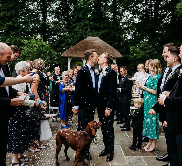 The two grooms are a kiss during their confetti exit with their pet dog 