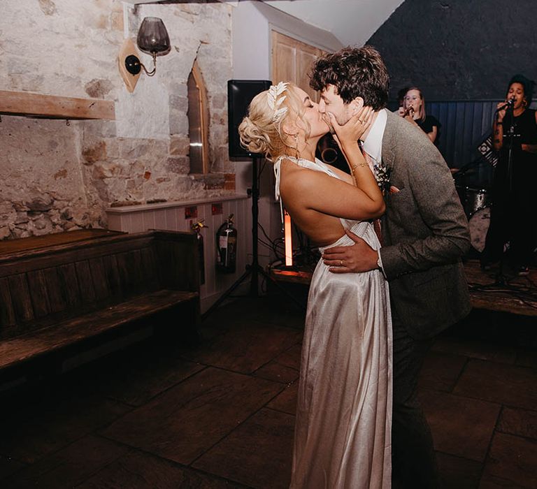 Bride wearing satin open back wedding reception dress with the groom in a grey tweed suit having their first dance together 