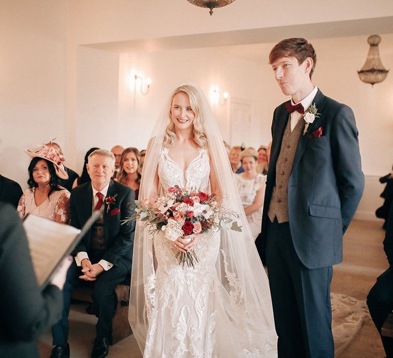 Winter wedding ceremony at Aswarby Rectory with the groom in navy suit with bride in embellished wedding dress and veil 