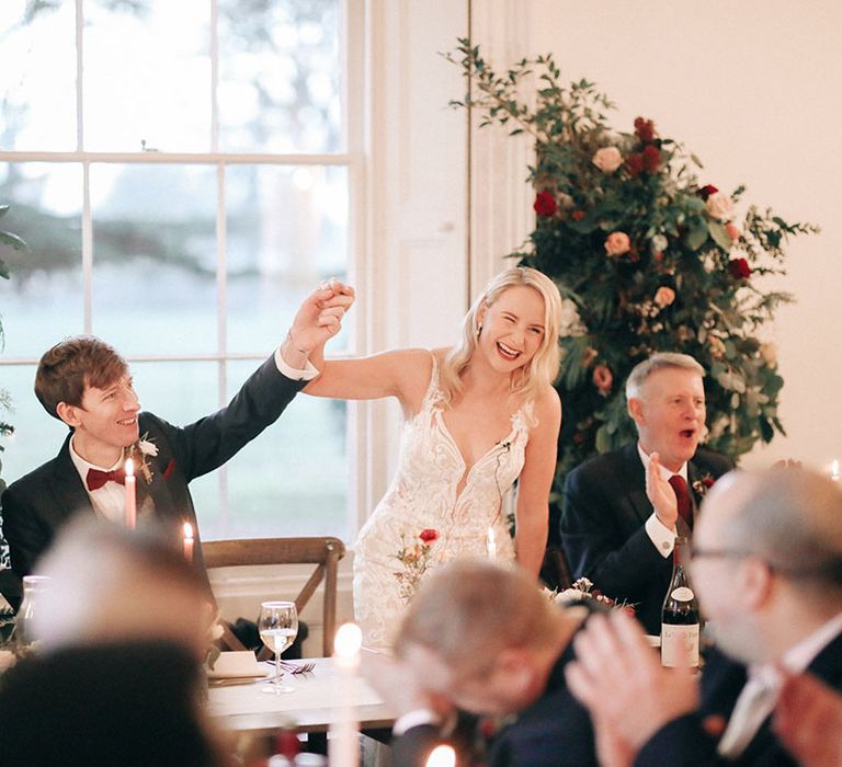 Bride and groom sit at their wedding breakfast in front of festive flower columns 