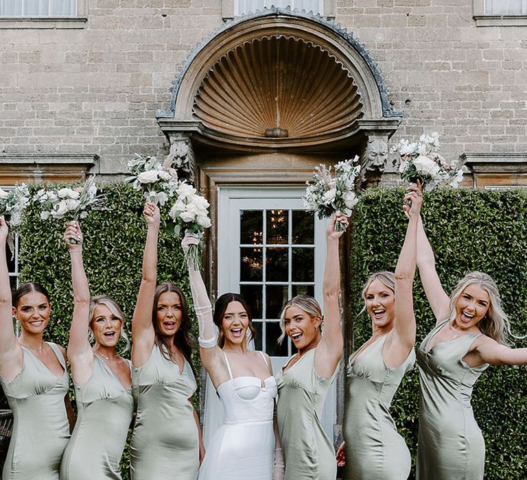 Bridal party with bridesmaids in sage green satin bridesmaid dresses with the bride holding white flower bouquets 