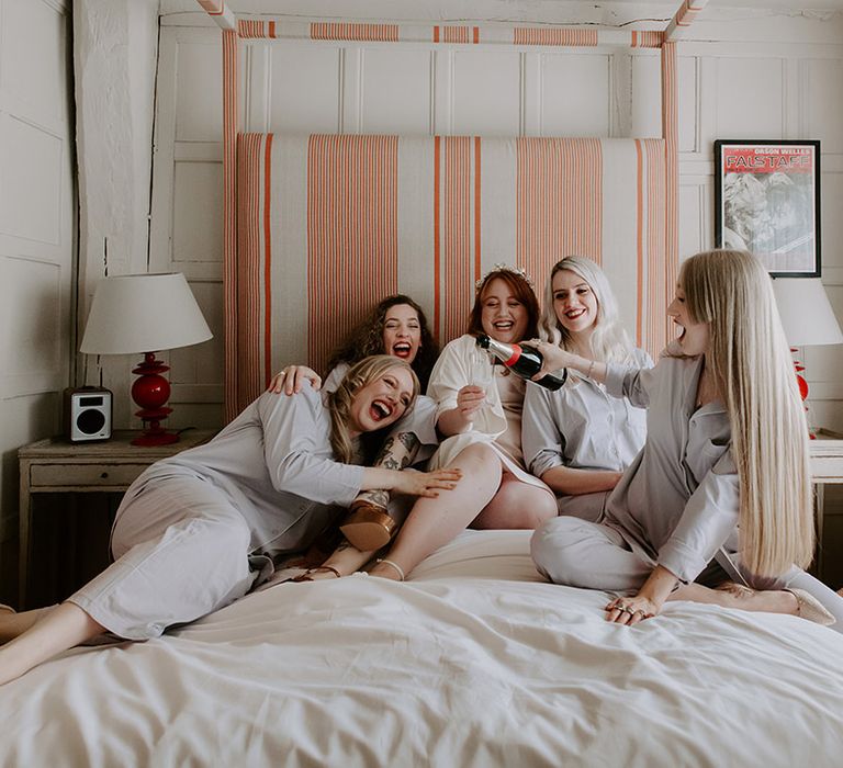 Bridal party on the bed laughing together as they get ready for the wedding day in matching grey and white pyjamas 