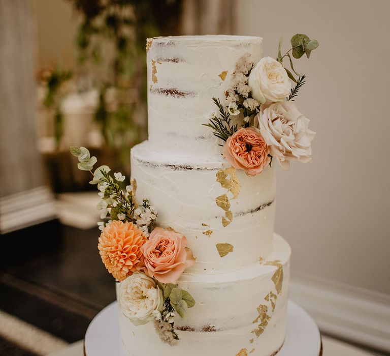 Three tier white iced rustic wedding cake decorated with orange and white flowers