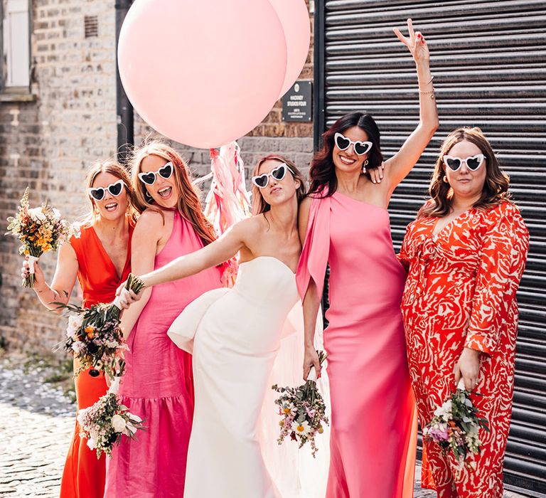 Bridal party wearing pink and orange mismatched bridesmaid dresses with large pink wedding balloons 