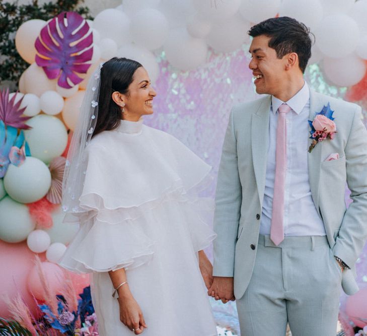 Bride in short wedding dress and boots and groom in pale green suit holding hands 