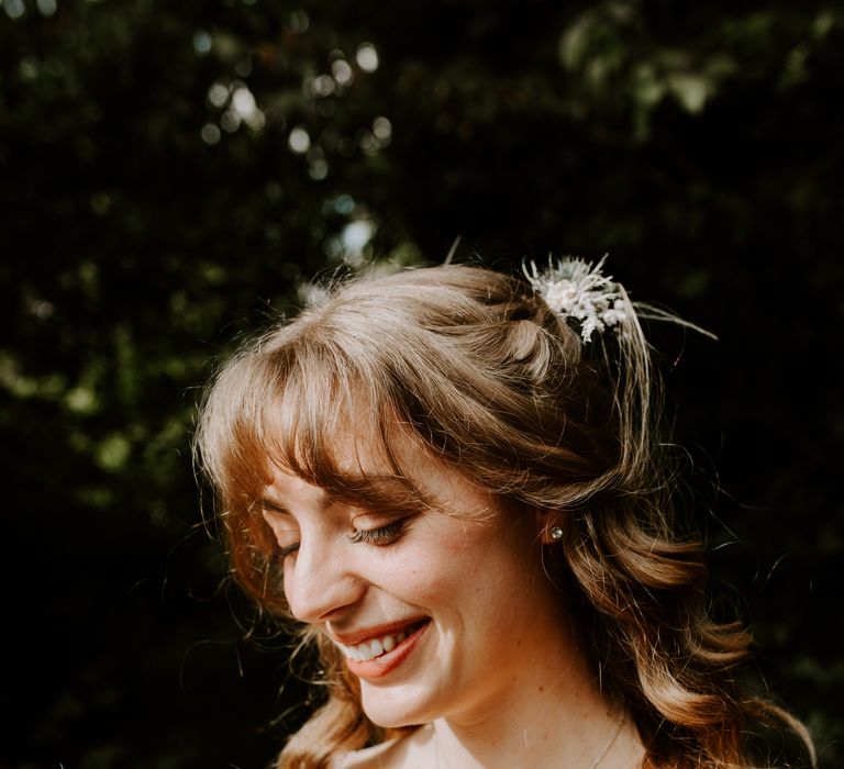 Wintery green and white dried flower bouquet held by smiling bride with matching hair pieces