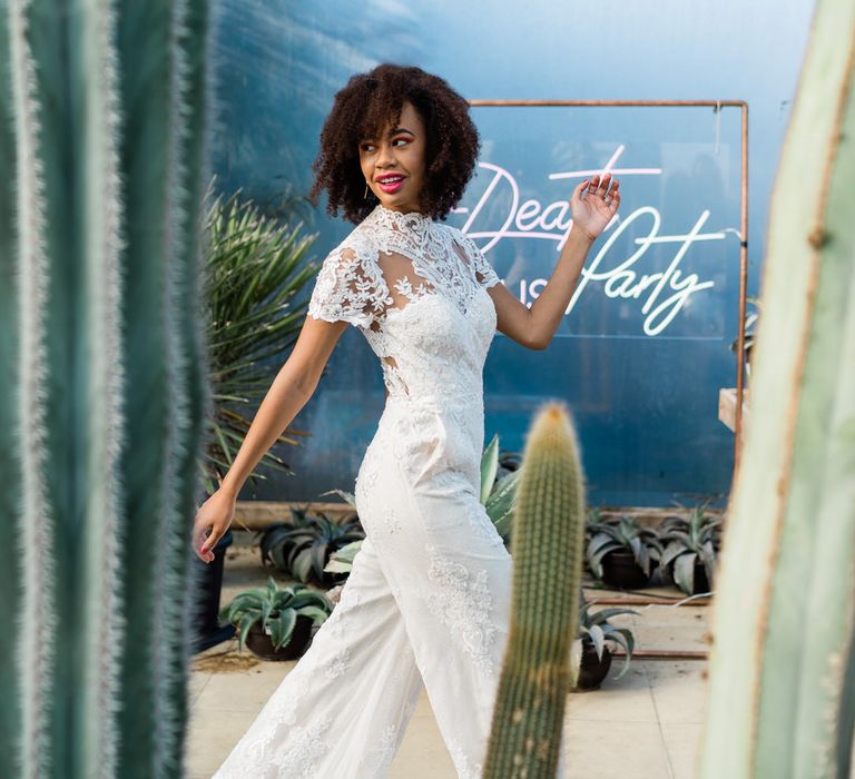 Bride in white jumpsuit walking past neon sign at Urban Jungle Suffolk 