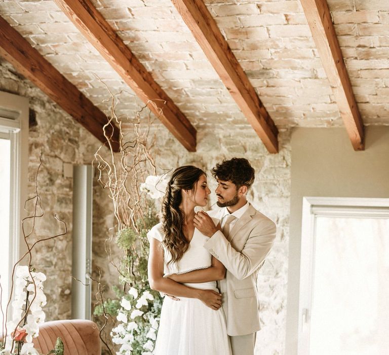 Beaded groom in a beige suit caressing his brides face standing on wicker rugs 