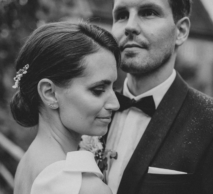 Bride in white Jesus Piero gown and cathedral length veil embraces groom in black Tiger of Sweden tux in gardens at German wedding with elegant details